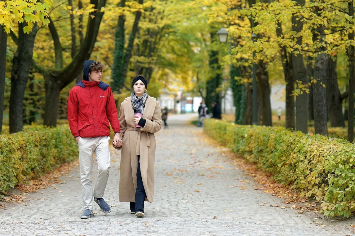 A man and woman walking side by side on a cobblestone path lined with golden autumn trees.