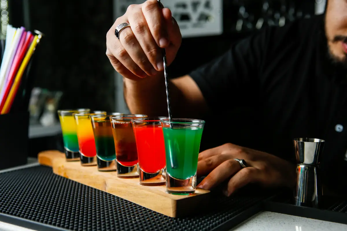 A bartender expertly stirring a lineup of colorful layered shots, showcasing cocktail mixing trends
