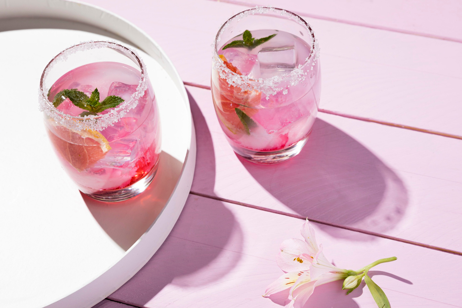 Two glasses of a pink Madame Butterfly-inspired cocktail, delicately garnished with mint on a sunlit table