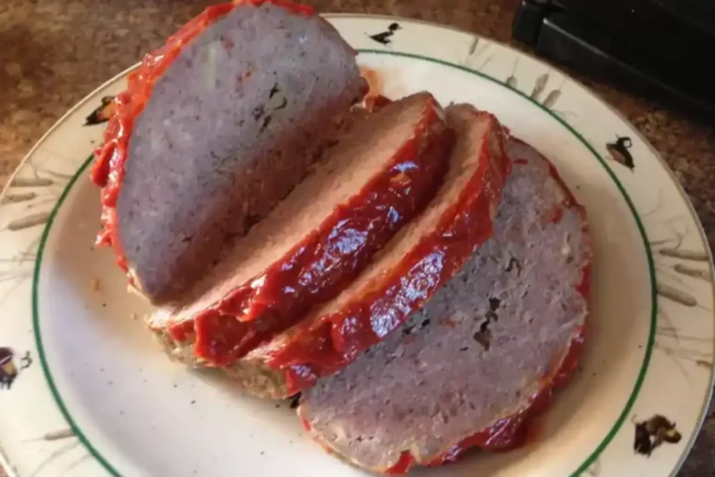 Slices of traditional Cracker Barrel meatloaf topped with a rich tomato glaze, served on a vintage patterned plate.