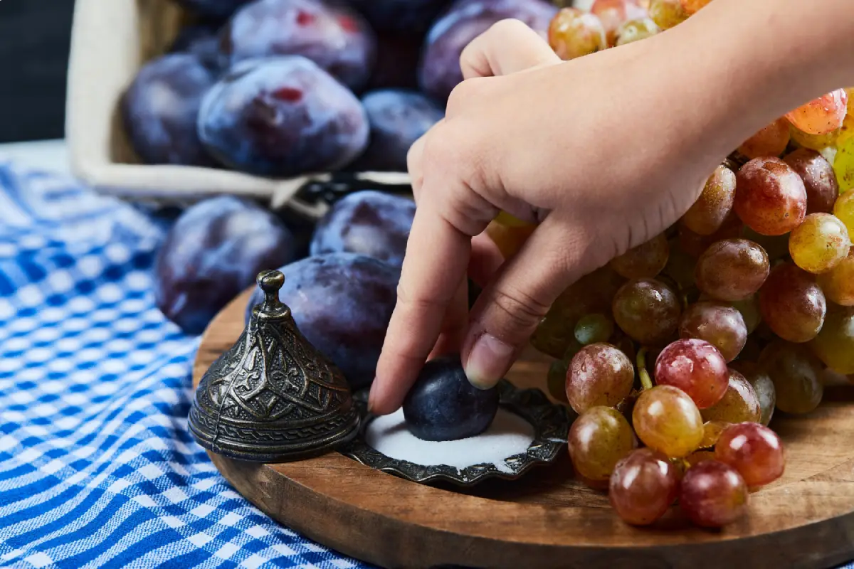 A hand picking a plum from a selection of fresh grapes and plums, reminiscent of the flavors of grape Jolly Ranchers