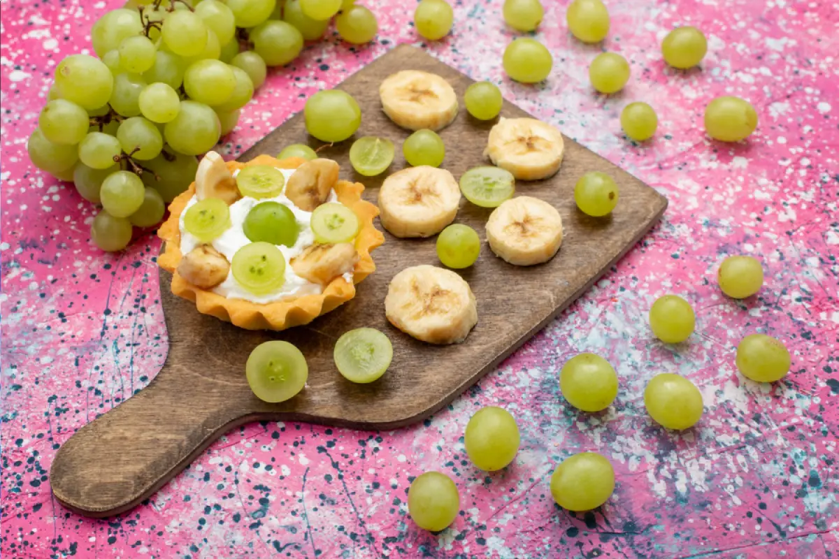 Fresh green grapes and banana slices on a dessert tart, on a colorful background