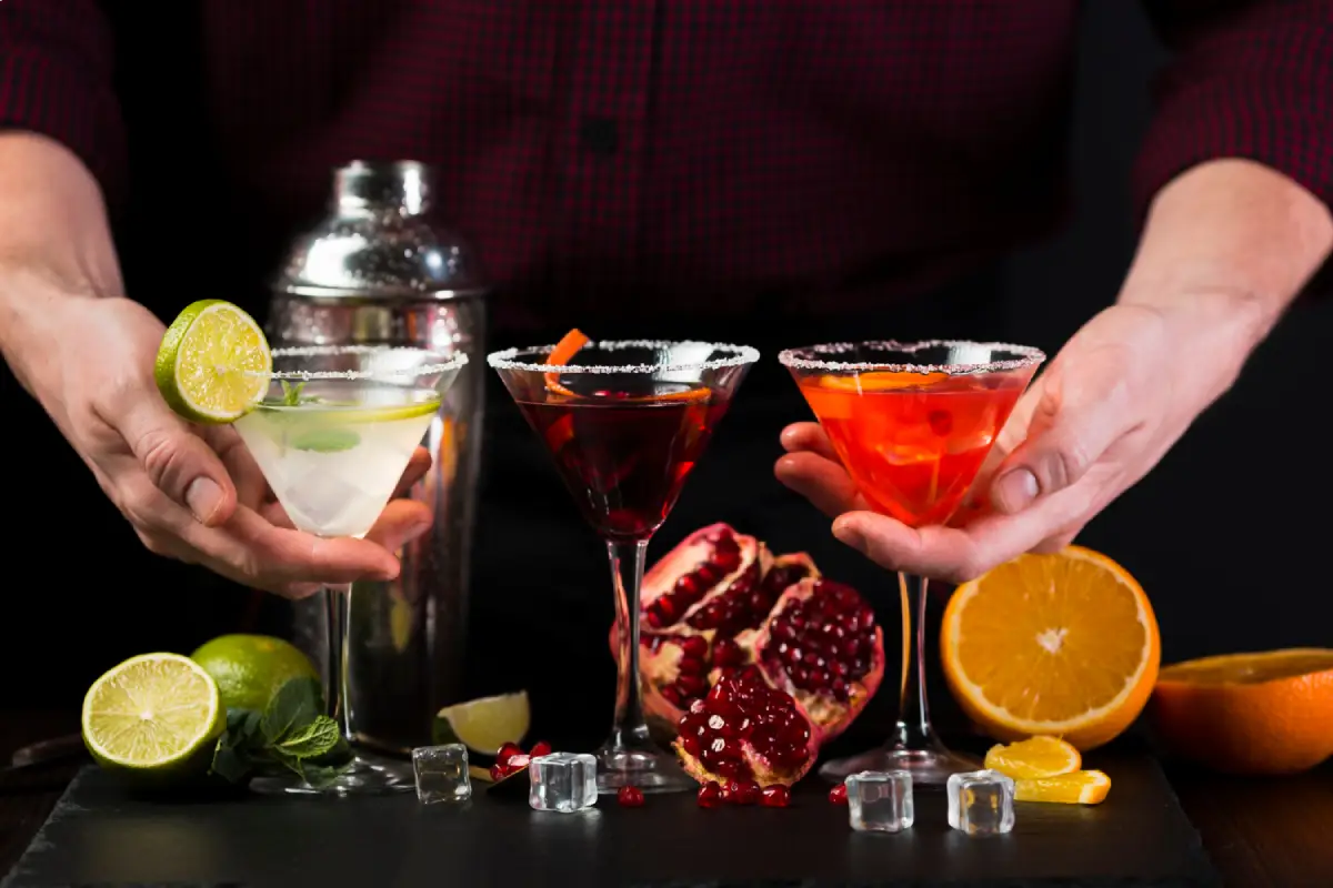 A bartender presenting three different cocktails, garnished with citrus fruits
