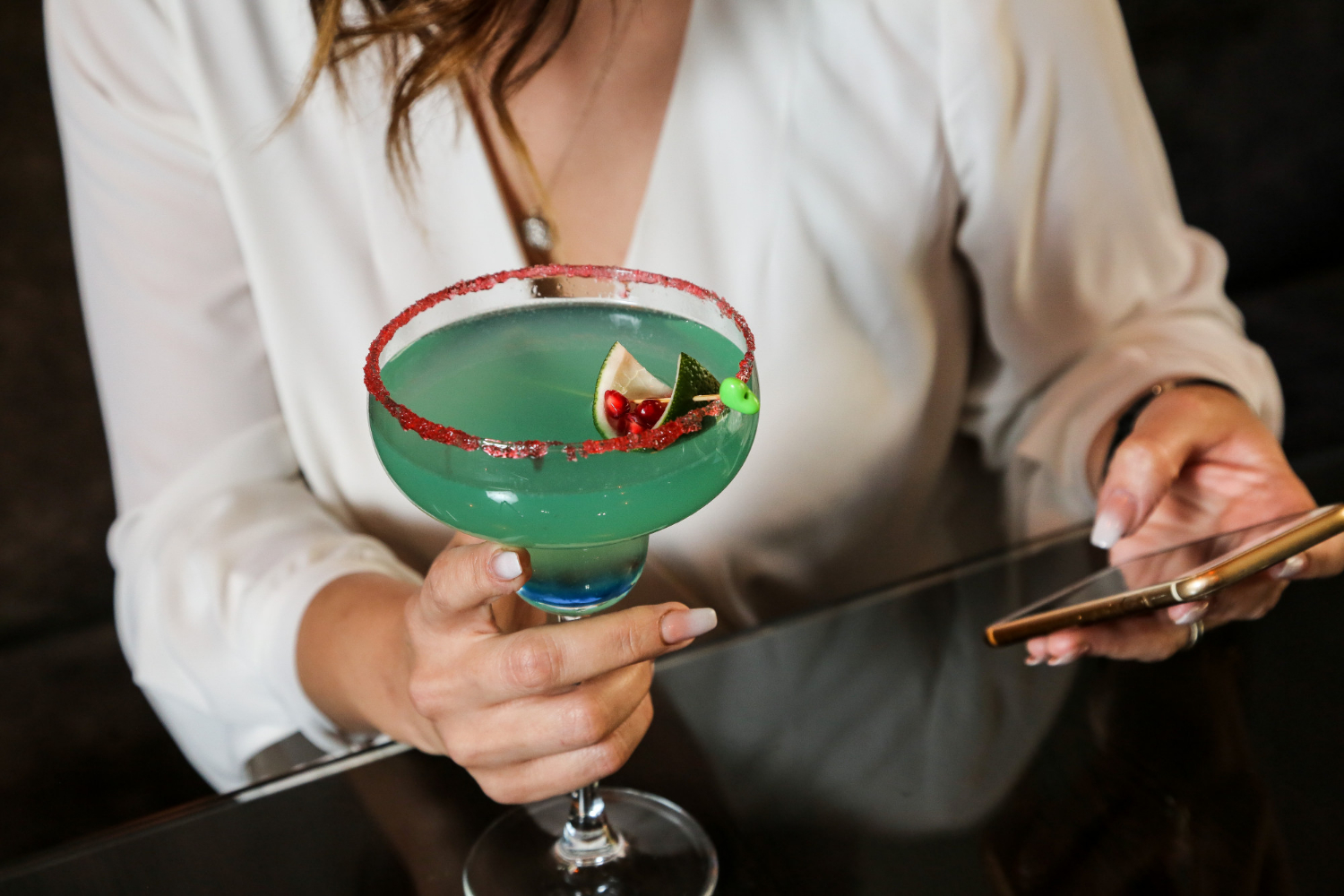A woman holding a vibrant green cocktail garnished with lime and pomegranate, reminiscent of the Madame Butterfly opera