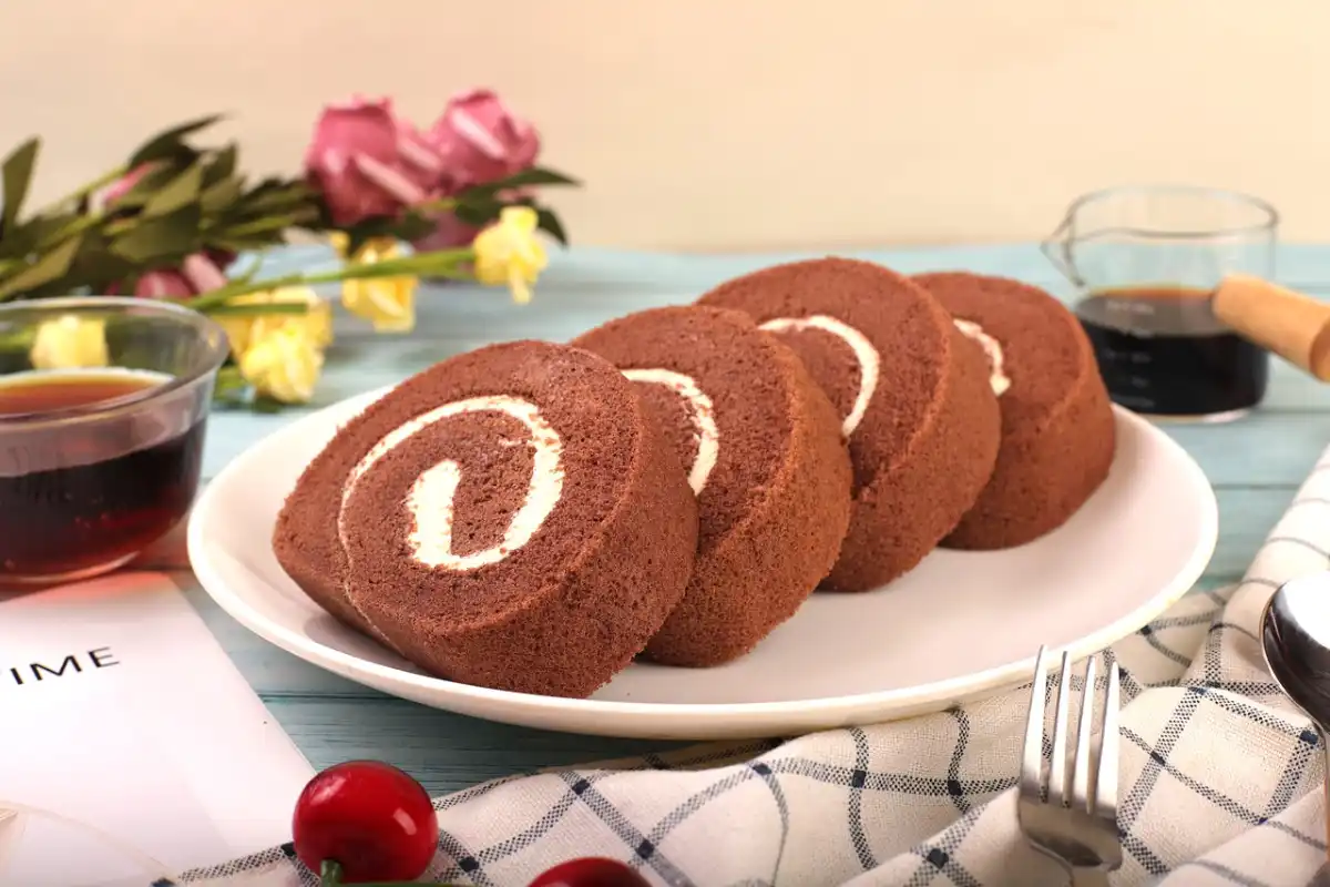 Slices of chocolate Swiss roll with creamy filling on a platter among various pastries.