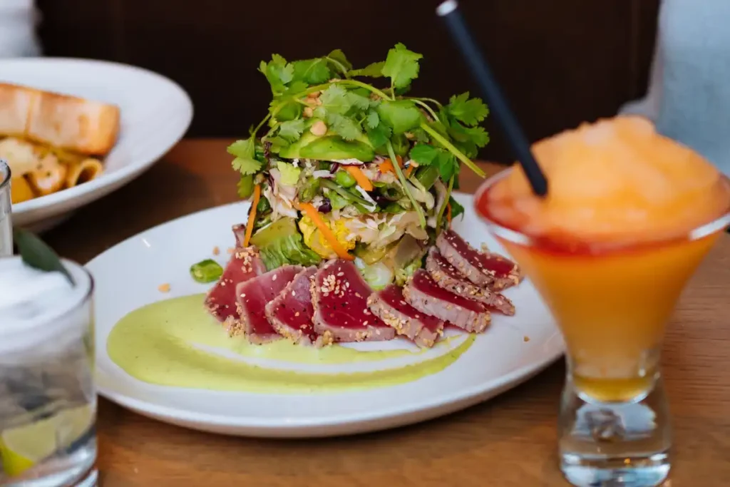 Japanese tuna salad featuring seared tuna slices and a vibrant vegetable tower, served with a creamy wasabi dressing and a refreshing cocktail.