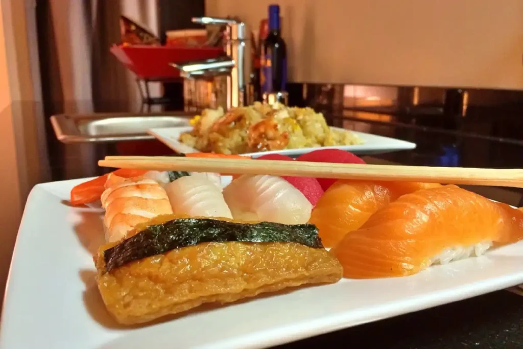 A colorful and beautifully arranged plate of chirashi sushi, featuring a variety of fresh sashimi, sliced vegetables, and garnishes atop a bed of vinegared sushi rice. The sushi is presented in an elegant, wooden sushi boat-shaped platter, with chopsticks and a bowl of soy sauce on the side.