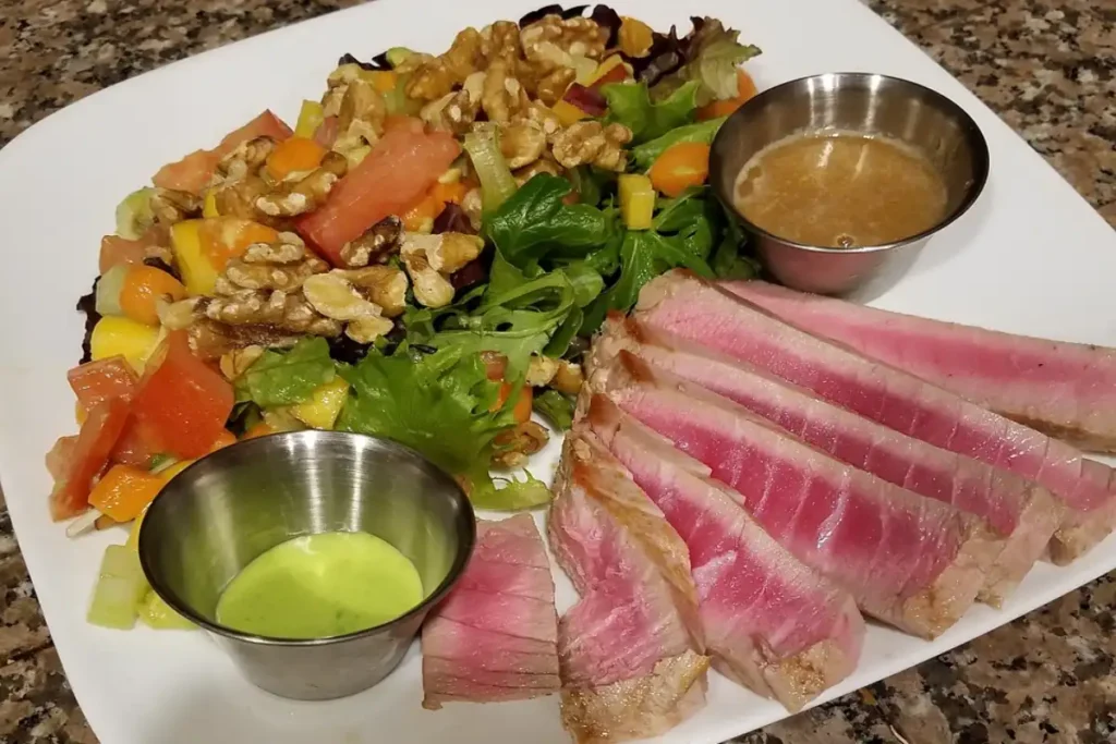 Succulent slices of seared tuna alongside a colorful mixed greens salad with tomatoes, carrots, mango, and walnuts, served with two dressings.