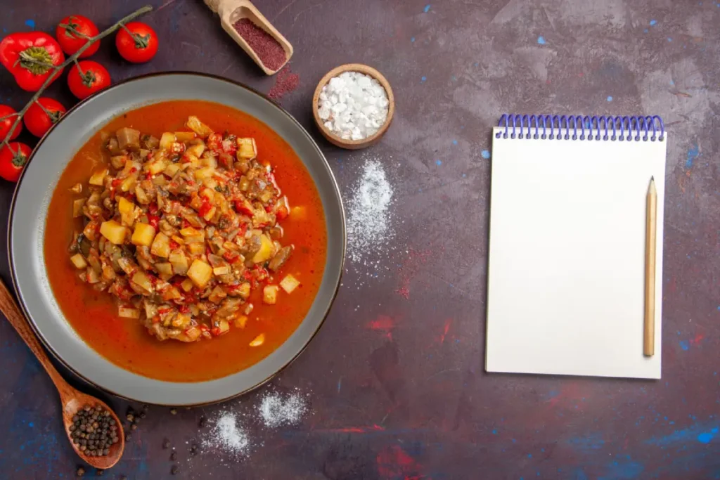 A bowl of hearty vegetable soup next to fresh ingredients and a notepad, for "Busy Day Soup Recipe.