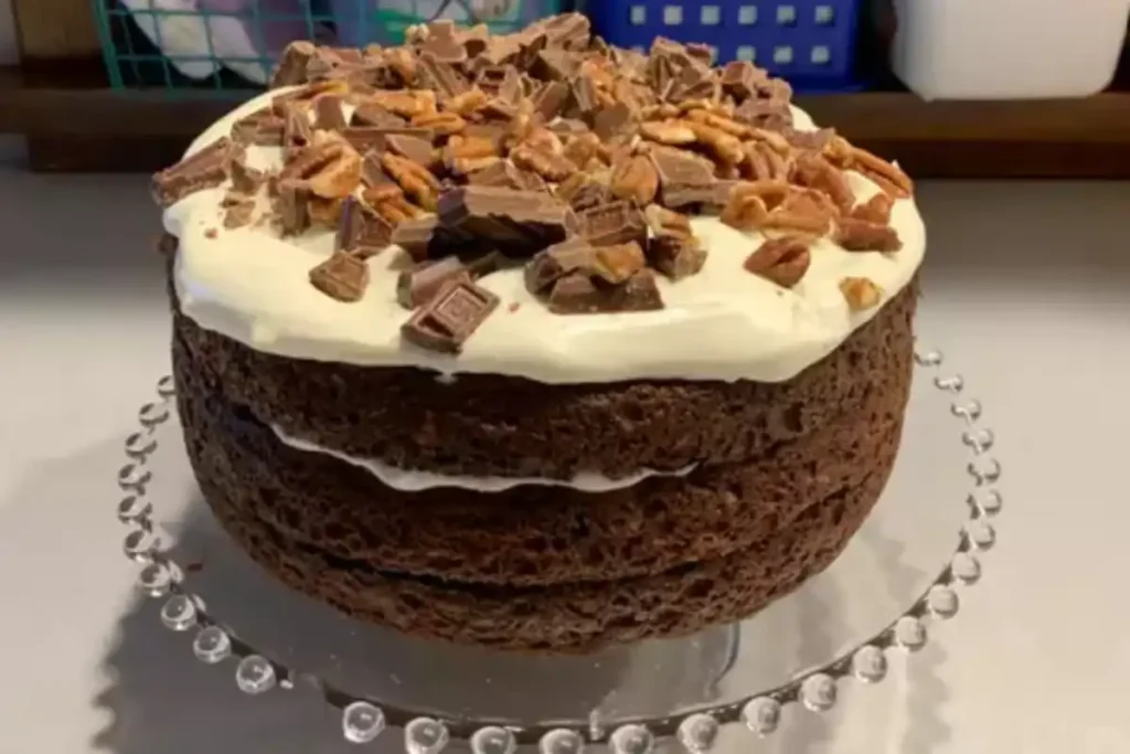 candy bar cake topped with chunks of chocolate and nuts on a creamy white frosting.