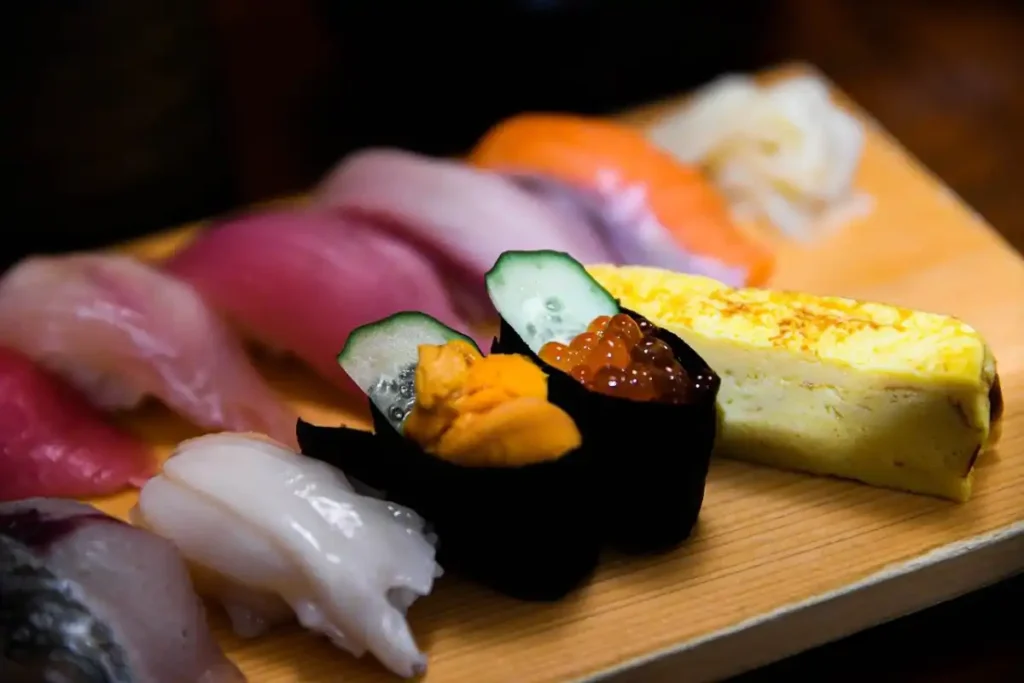 Assorted nigiri sushi selection featuring slices of raw fish, uni, ikura, and tamago on a wooden serving board.