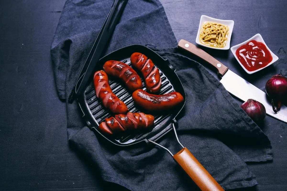 Juicy sausages sizzling in a grill pan with condiments on the side