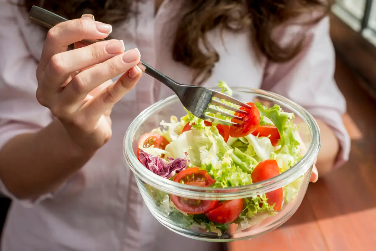 A woman enjoying a bowl of dairy-free salad, focusing on fresh ingredients