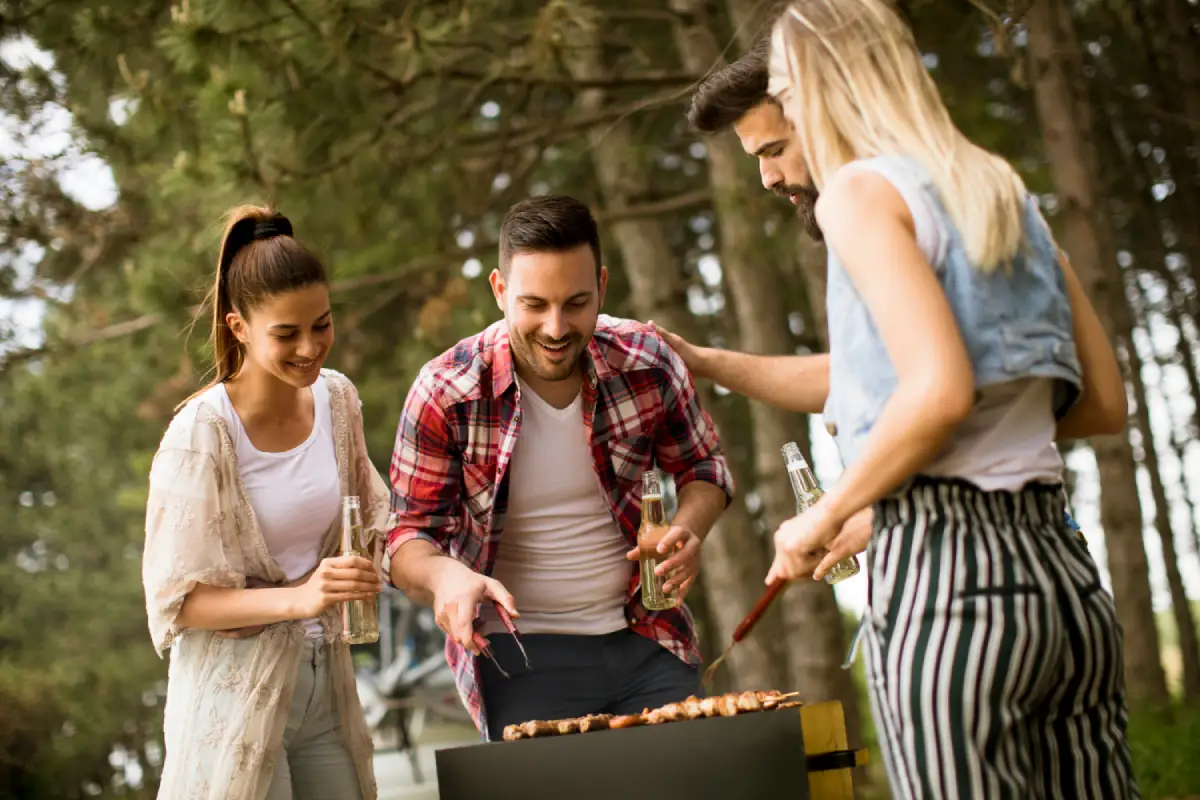 Friends gathering around a barbecue, cooking red hot sausages