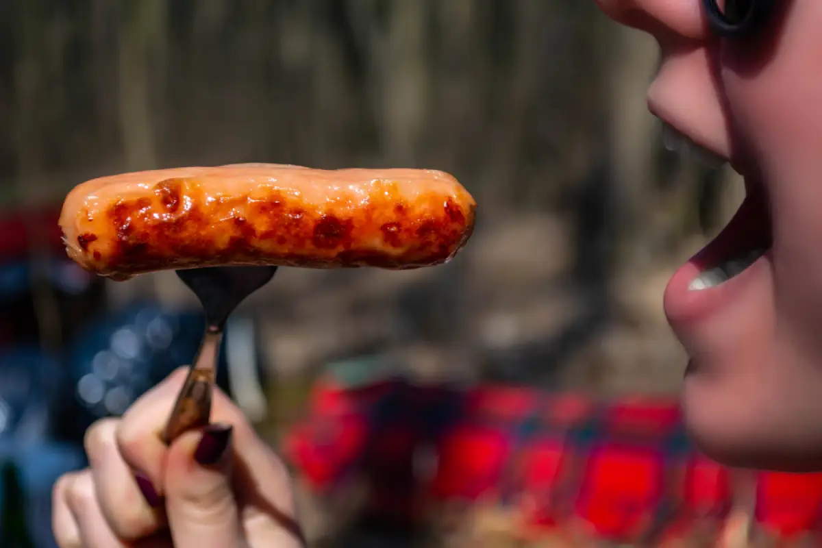 Person about to enjoy a freshly grilled Red Hots sausage on a fork.
