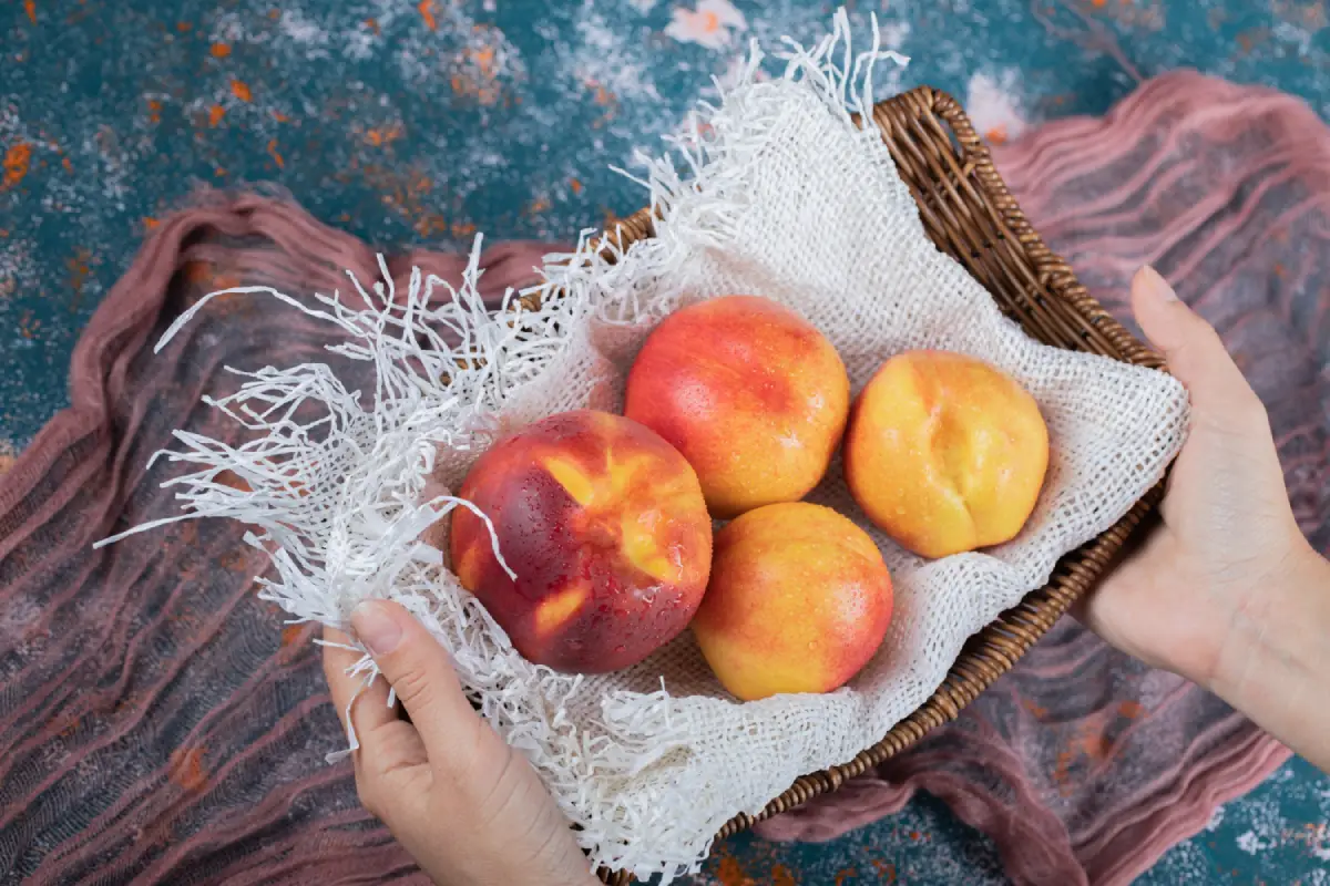Ripe yellow peaches in a basket on a rustic kitchen towel, ready for peach cobbler.