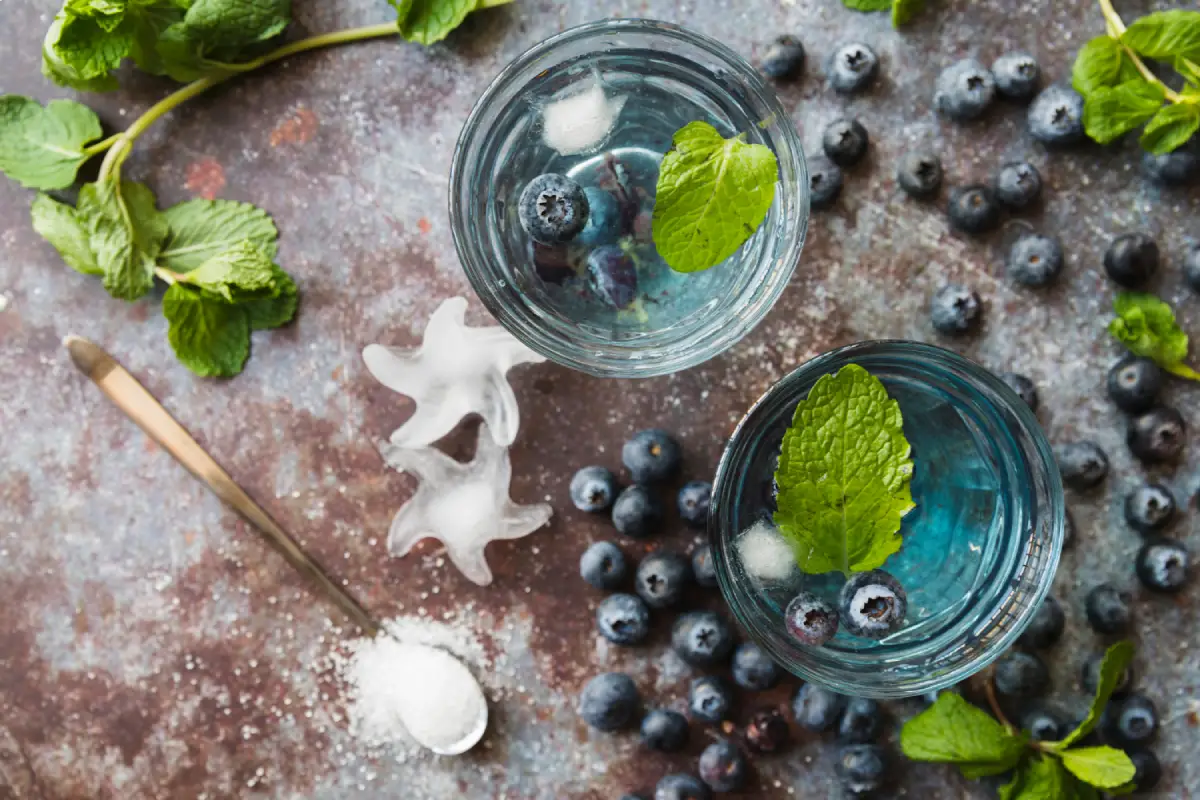 Two glasses of a refreshing drink with blueberries and mint leaves on a rustic surface