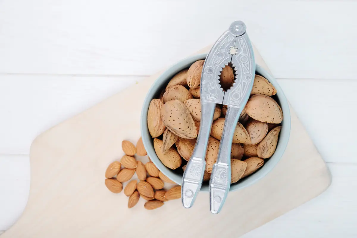 Nutcracker resting on a bowl full of almonds on a wooden board.