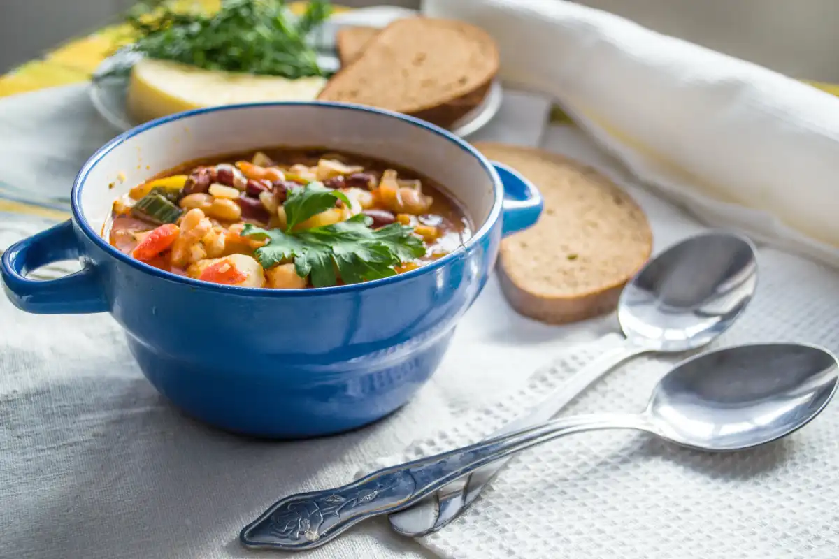 A hearty bowl of Italian-style bean and vegetable soup, served in a blue pot, garnished with fresh parsley.