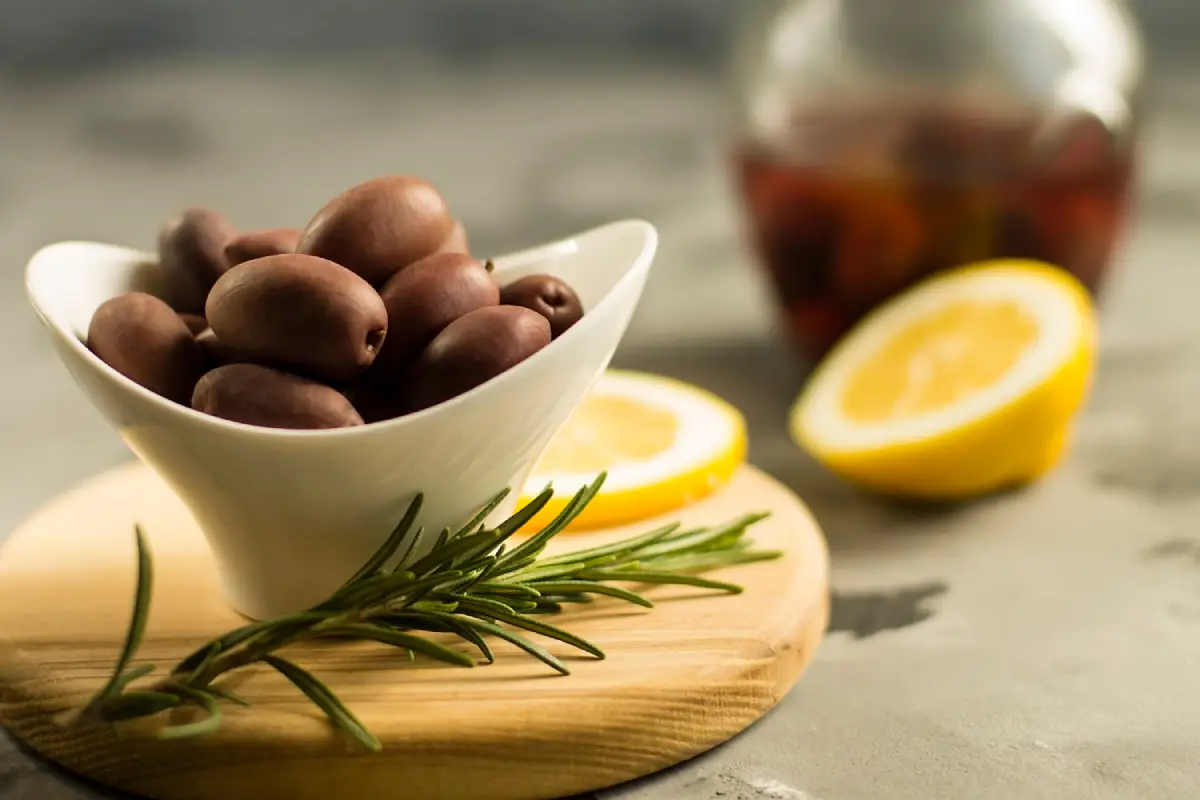 Bowl of Kalamata olives on a wooden board with rosemary and lemon slices