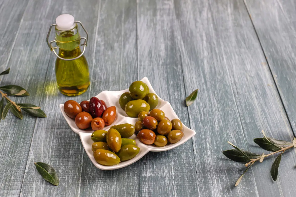 Assorted olives in a star-shaped dish with olive oil and olive leaves on a wooden table