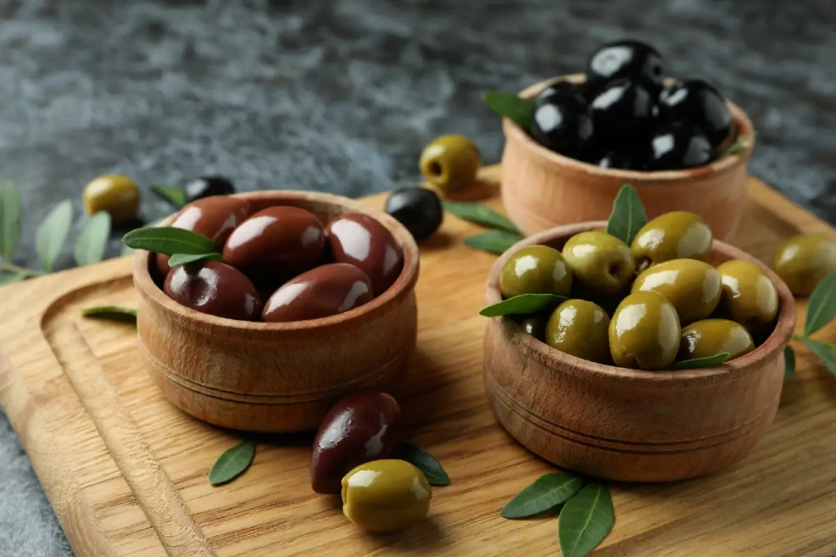 Assorted olives in wooden bowls on a cutting board.