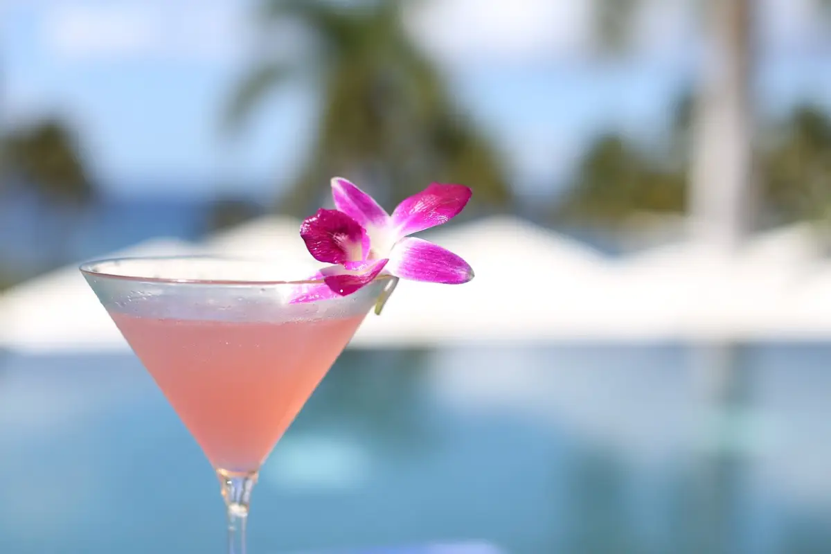 A Madame Butterfly cocktail garnished with a pink orchid by the pool