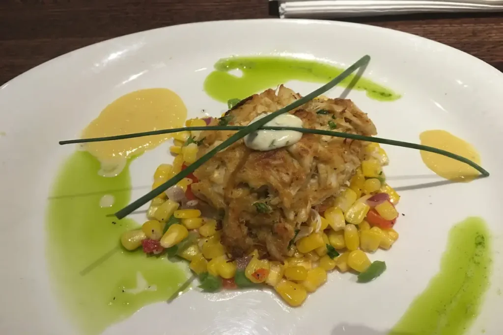 Gourmet air-fried crab cake on a bed of corn relish with artistic sauce garnish