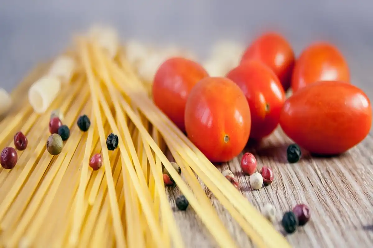 Exploring the essence of Italian cuisine with fresh ingredients, this image showcases spaghetti, cherry tomatoes, and peppercorns on a rustic wooden surface.