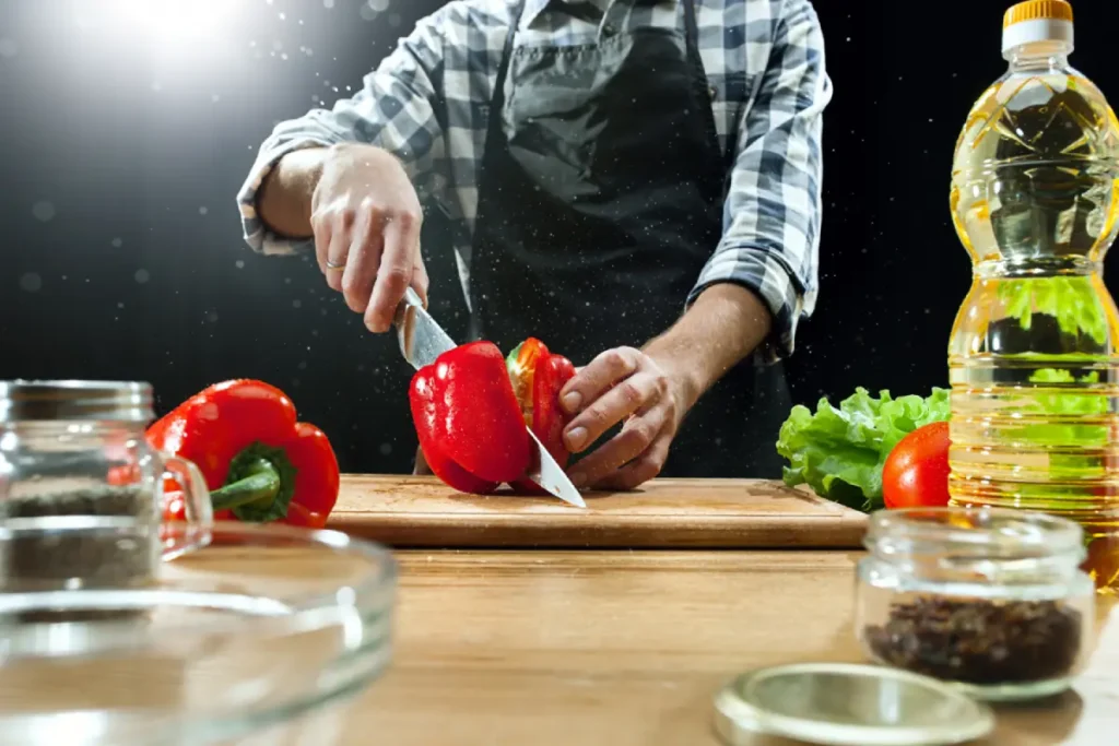 Chef preparing soup in advance by slicing red bell peppers on a wooden board