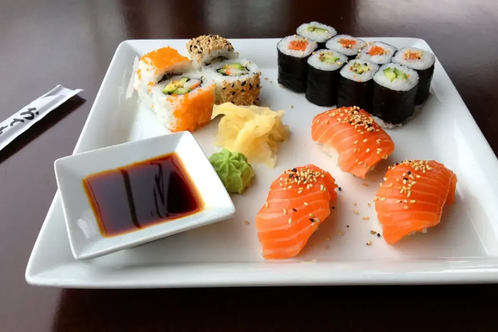 Assorted sushi and salmon sashimi plate with soy sauce and condiments.