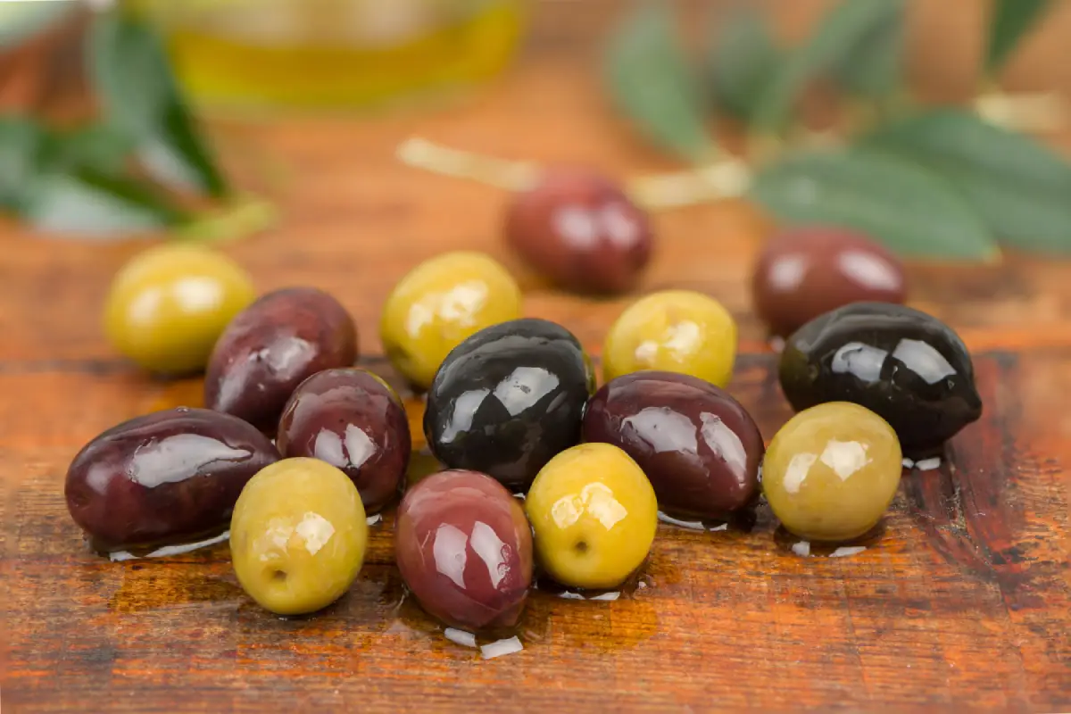 Mixed Kalamata and green olives with olive leaves on a rustic wooden table.