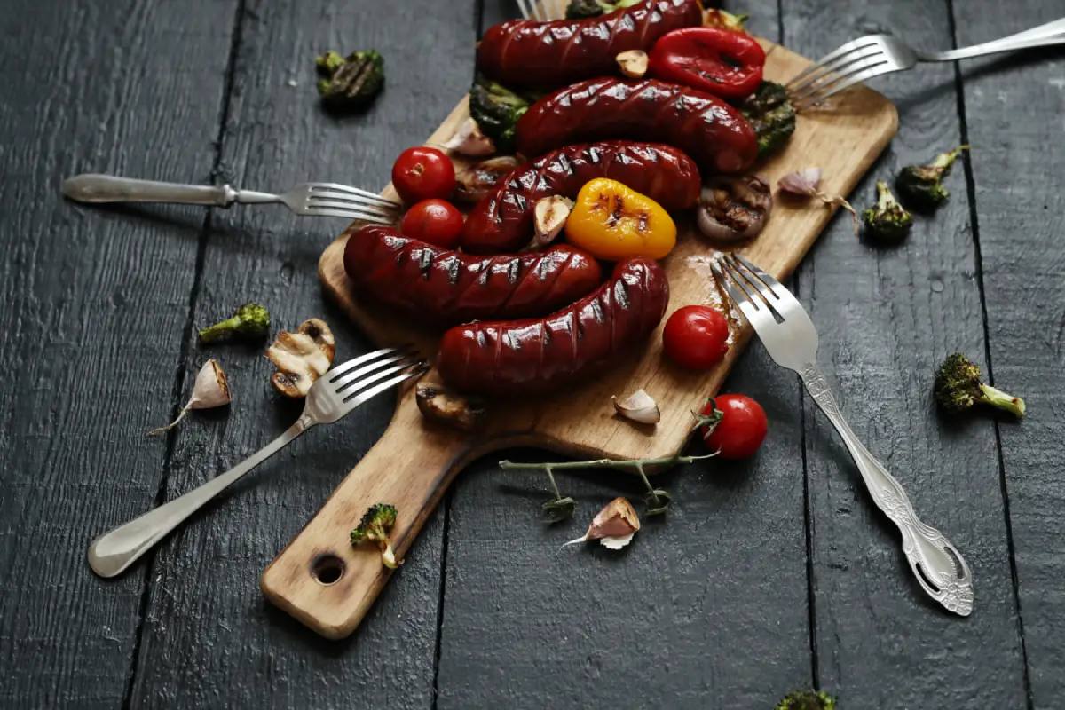 Grilled sausages served on a wooden board with roasted vegetables