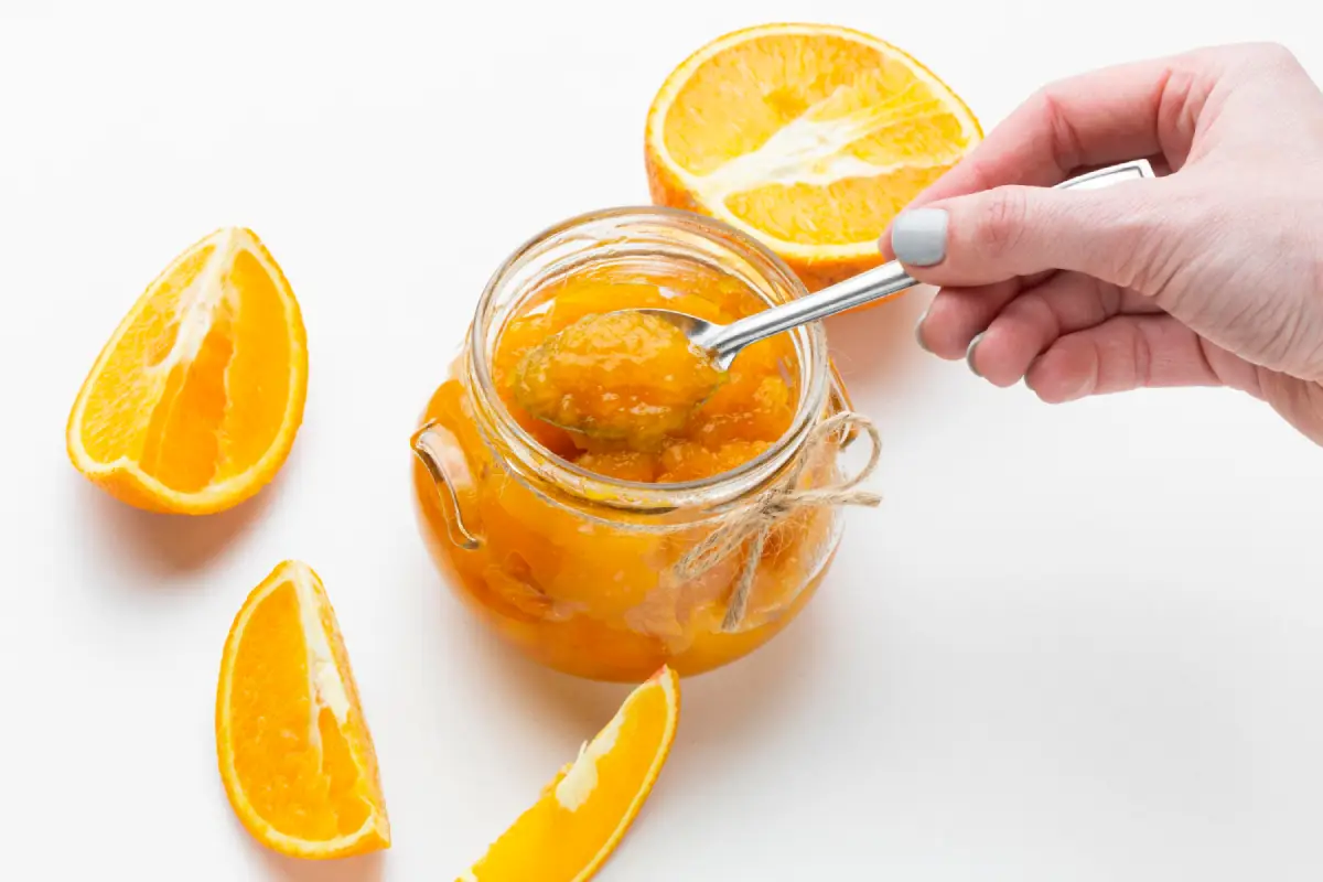 Hand scooping orange preserve from a jar, illustrating a step in storing Orange Dreamsicle Salad