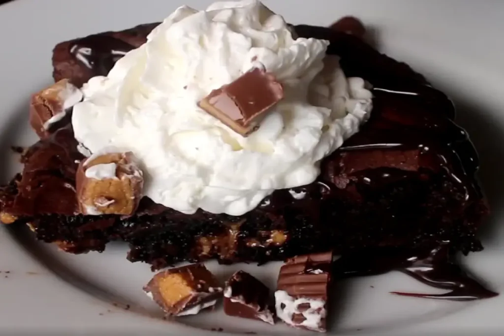 A rich and gooey peanut butter cup dump cake topped with whipped cream and drizzled with chocolate syrup.