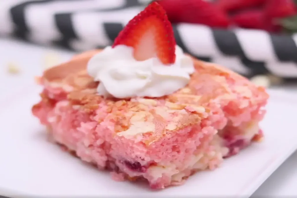 A slice of Strawberry Earthquake Cake topped with a dollop of whipped cream and a fresh strawberry.