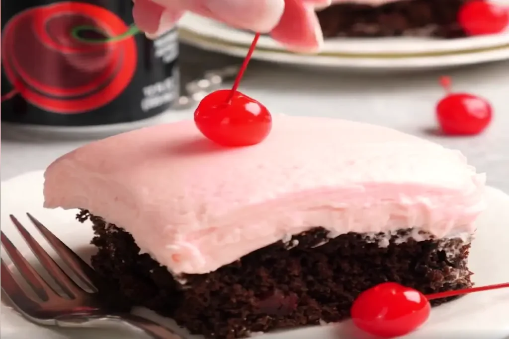 A slice of Cherry Dr. Pepper Chocolate Cake topped with a pink cherry frosting and a maraschino cherry.