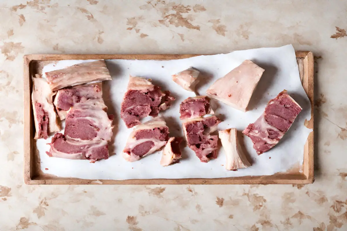  Assorted cuts of beef bones on a wooden tray, showcasing the variety for broth making.