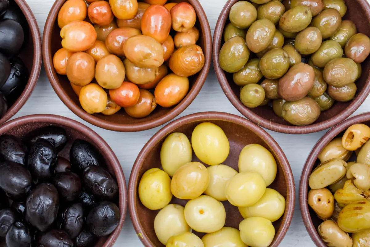 Close-up of assorted olives in clay bowls on a white wooden surface.
