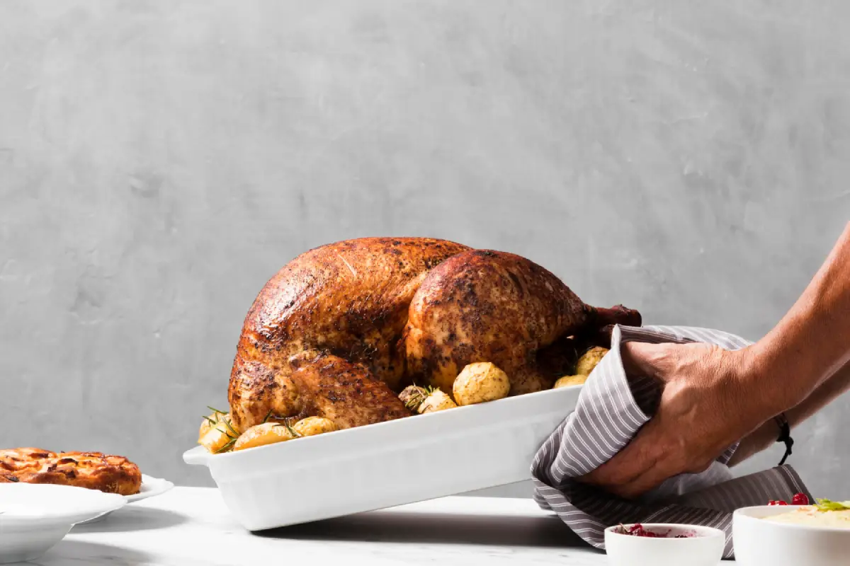 Hands placing a perfectly roasted turkey on the table, demonstrating the results of proper basting frequency