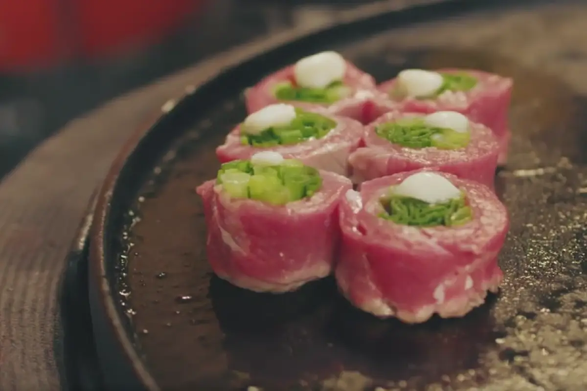 Beef Negimaki rolls with scallions and cheese on a hot griddle.
