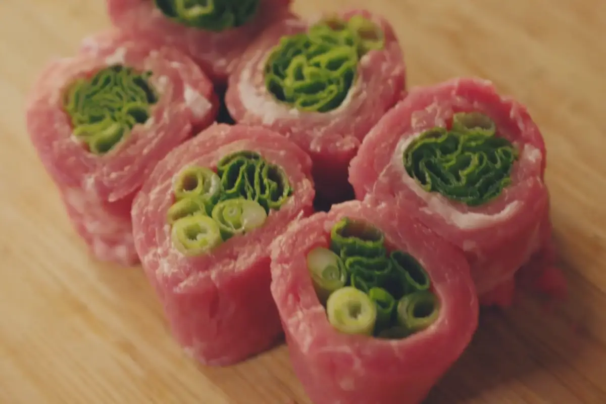 Raw beef rolls filled with green scallions, prepared for cooking.