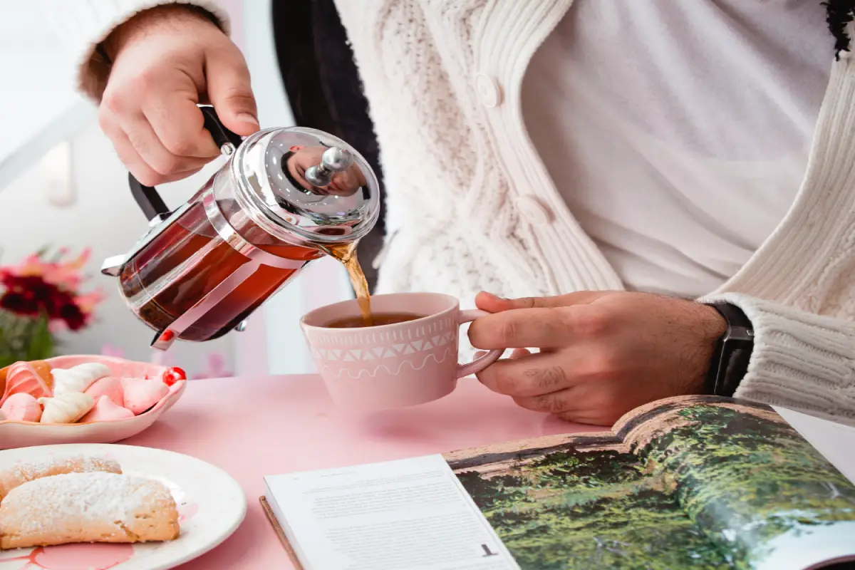 Man pouring a cup of Earl Grey tea from a teapot, accompanying a tea-time spread.