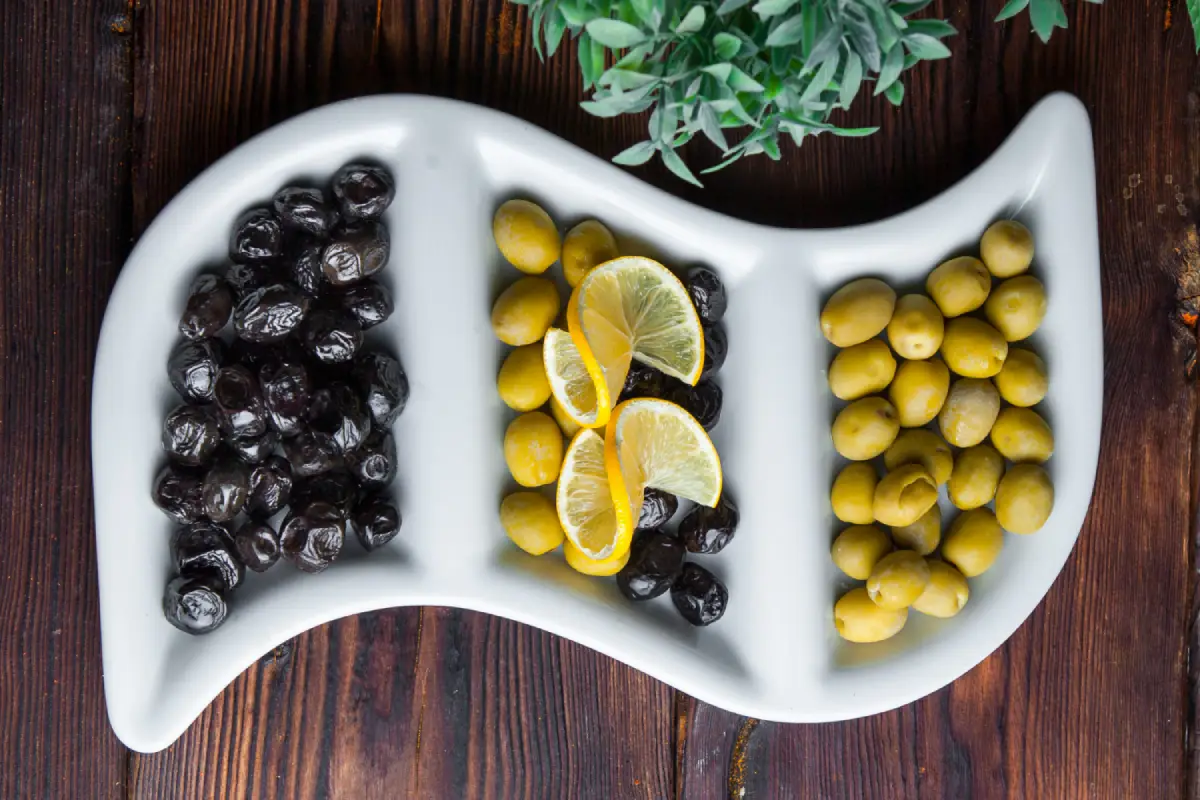 Black and green olives with lemon slices on a yin-yang shaped plate, symbolizing balance.