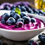 Fresh blueberries on top of a vibrant purple blueberry cream cheese spread in a white bowl.