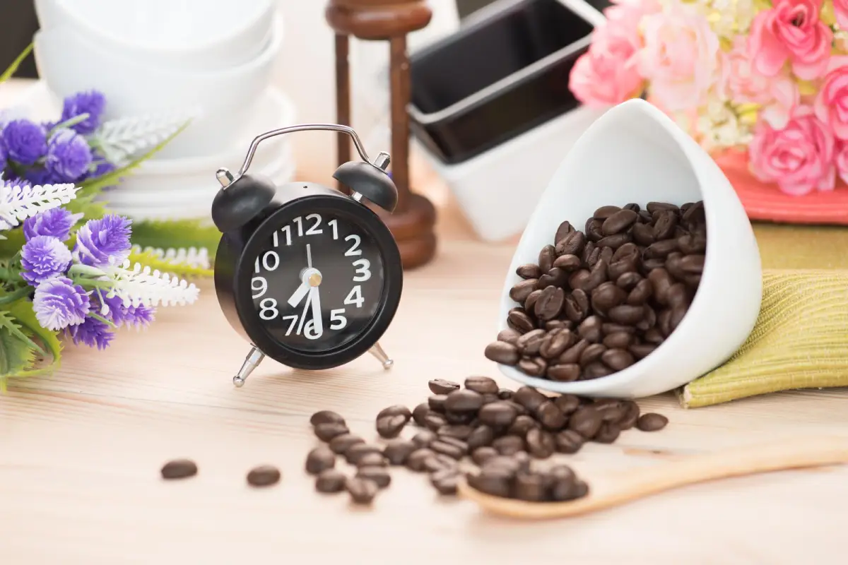 Coffee beans spilled beside a classic alarm clock and flowers