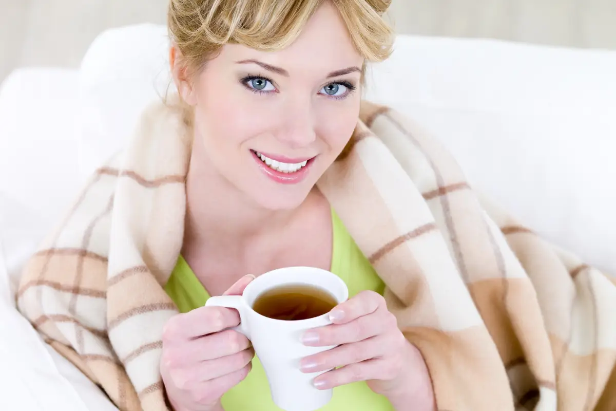 Smiling woman enjoying a warm cup of tea while wrapped in a cozy blanket