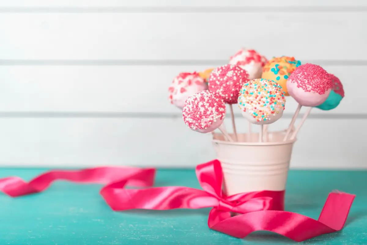 A bouquet of colorful Valentine cake pops decorated with sprinkles and a pink ribbon
