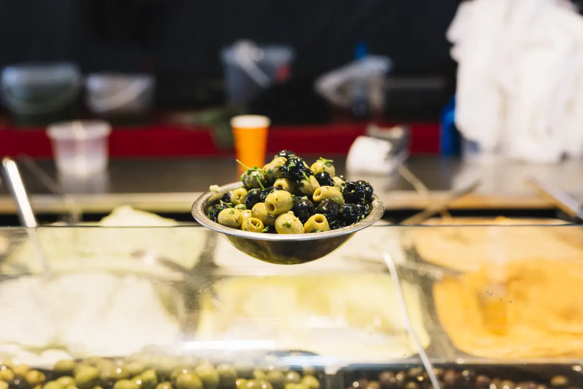 A bowl of mixed black and green olives on a glass counter, showcasing diverse olive flavors for culinary use.