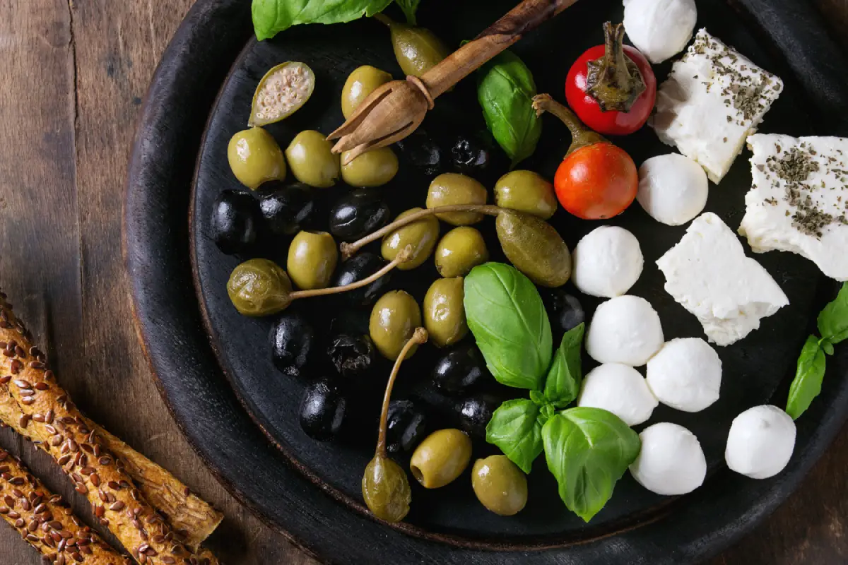 Mediterranean appetizer plate with Kalamata olives, cheese, tomatoes, and basil.